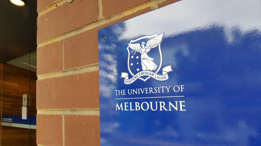 A photograph of a sign in front of a brick wall with the University of Melbourne logo on it.